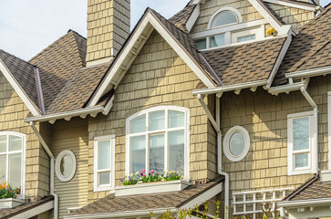 Top of grey stucco luxury house with shingle roof, red and yellow trees and nice windows in Summer in Vancouver, Canada, North America. Day time on June 2024.
