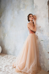 A beautiful girl in a long elegant beige gold wedding dress stands on the sand. Portrait of a beautiful bride on a gray background. Bright make-up and bundle styling. Gorgeous brunette woman