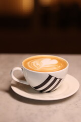 A beautifully crafted cup of cappuccino with latte art, served in an elegant white porcelain cup with a stylish design, placed on a marble table.