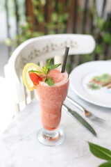 Strawberry and lemon slush garnished with fresh mint, a lemon slice, and a strawberry wedge, served in a tall glass on a marble table.