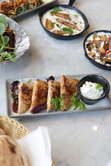 A plate of Lebanese arais, grilled flatbread stuffed with savory chicken filling, served alongside a creamy labneh dip and fresh greens, offering a delicious Middle Eastern appetizer.