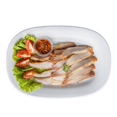 Sliced meat served on a white platter with garnishes of lettuce, tomato, and a small bowl of chili flakes.