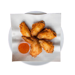 Crispy fried chicken wings arranged neatly on a plate accompanied by a small cup of dipping sauce.