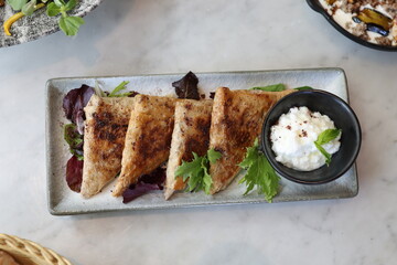 A plate of Lebanese arais, grilled flatbread stuffed with savory chicken filling, served alongside a creamy labneh dip and fresh greens, offering a delicious Middle Eastern appetizer.
