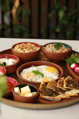 A traditional Lebanese breakfast spread featuring fried eggs, zaatar, hummus, labneh, butter, apricot jam, fresh vegetables, olives, and Lebanese bread, beautifully arranged on a rustic tray.