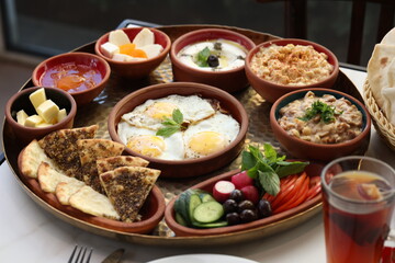 A traditional Lebanese breakfast spread featuring fried eggs, zaatar, hummus, labneh, butter, apricot jam, fresh vegetables, olives, and Lebanese bread, beautifully arranged on a rustic tray.