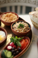 A traditional Lebanese breakfast spread featuring fried eggs, zaatar, hummus, labneh, butter, apricot jam, fresh vegetables, olives, and Lebanese bread, beautifully arranged on a rustic tray.
