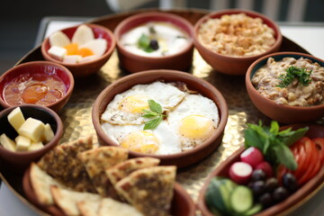A traditional Lebanese breakfast spread featuring fried eggs, zaatar, hummus, labneh, butter, apricot jam, fresh vegetables, olives, and Lebanese bread, beautifully arranged on a rustic tray.