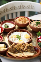 A traditional Lebanese breakfast spread featuring fried eggs, zaatar, hummus, labneh, butter, apricot jam, fresh vegetables, olives, and Lebanese bread, beautifully arranged on a rustic tray.