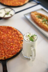 A traditional Lebanese manoushe topped with seasoned minced meat, served on a black tray beside a glass of laban yogurt drink, presented on a marble table.