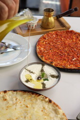 A traditional Lebanese breakfast spread featuring tomato manoushe, cheese manoushe, and a bowl of creamy labneh garnished with an olive and dried herbs, served on a rustic setup.