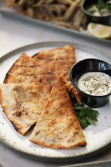 Crispy lahmacun slices filled with minced meat and herbs, served on a white plate with a side of dipping sauce, offering a savory treat.