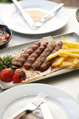 A platter of chargrilled Lebanese beef kebabs served with crispy French fries, grilled tomatoes, onions, fresh parsley, and sumac seasoning on flatbread, offering a hearty and flavorful Middle Eastern