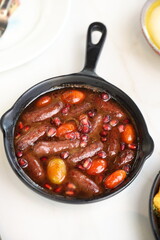 Makanek Lebanese sausages served in a black skillet with pomegranate seeds and cherry tomatoes, offering a vibrant and flavorful presentation.