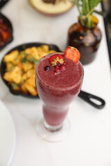 A vibrant berry smoothie topped with fresh strawberry and pomegranate garnish, served on a light table setup with a gourmet touch.