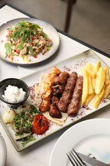 A Lebanese mixed grill platter featuring chargrilled beef kebabs, chicken skewers, and lamb skewers, served with French fries, garlic sauce, grilled tomatoes, fresh parsley, and sumac on flatbread, of