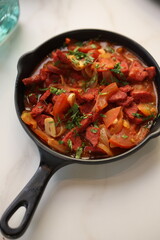 A skillet of spicy Lebanese soujouk sausages cooked with sautéed onions, tomatoes, and garlic in a rich, tangy tomato-based sauce, garnished with fresh parsley, delivering a bold and flavorful Middle 