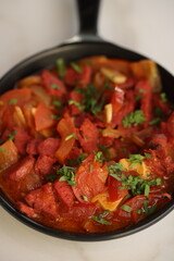 A skillet of spicy Lebanese soujouk sausages cooked with sautéed onions, tomatoes, and garlic in a rich, tangy tomato-based sauce, garnished with fresh parsley, delivering a bold and flavorful Middle 