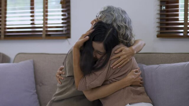 Daughter hugging her senior mother on the sofa, expressing love and care in a warm living room setting