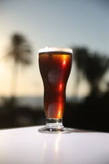 A rich, dark brew served in a tall glass, illuminated by the golden hues of a tropical sunset, offering a blend of sophistication and relaxation.