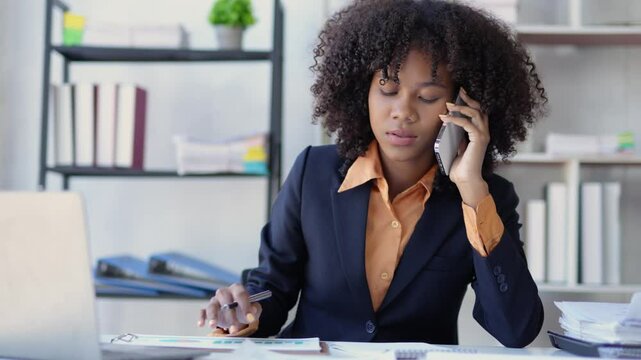 Businesswoman is multitasking at her desk, talking on her phone while simultaneously taking notes on a document