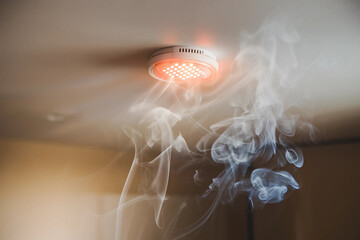Fire alarm evacuation monitoring concept. A smoke detector emits light as smoke swirls around it, indicating potential danger in the environment.