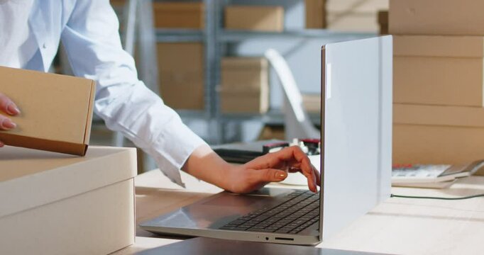 Small business owners working in warehouse checking stock inventory for shipping merchandise. Woman preparing order for client sitting at desk with laptop in storeroom. Online store concept. 4k video