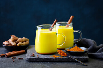 Turmeric latte, tea, golden milk in glass mugs with cinnamon. Grey background. Copy space.