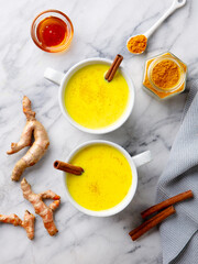Turmeric latte, tea, golden milk in cups with cinnamon. Marble background. Close up. Top view.