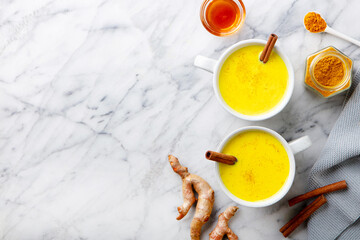 Turmeric tea, latte, golden milk in cups with cinnamon and fresh roots turmeric. Marble background. Copy space. Top view.