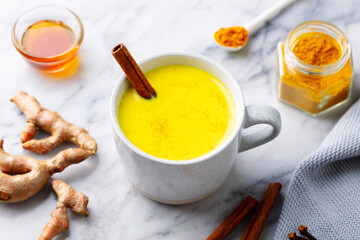 Turmeric latte, tea, golden milk in cups with cinnamon. Marble background. Close up.