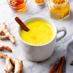 Turmeric latte, tea, golden milk in cups with cinnamon. Marble background. Close up.