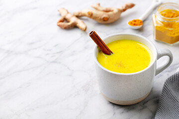 Turmeric tea, latte, golden milk in cups with cinnamon and fresh roots turmeric. Marble background. Close up. Copy space.