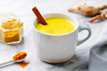 Turmeric latte, tea, golden milk in cups with cinnamon and fresh roots turmeric. Marble background. Close up.
