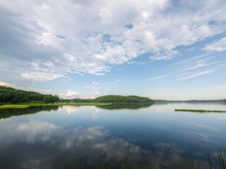 Fototapeta premium Reflections of the sky on a calm lake surface amidst lush green surroundings, parkland views, landscape photography