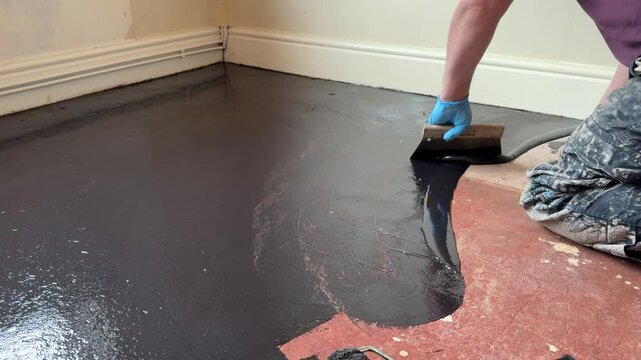 Unidentified worker uses a trowel to apply damp proof membrane coating to a floor
