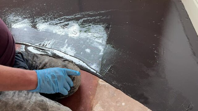 Unidentified man uses a trowel to apply damp proof membrane coating to a floor