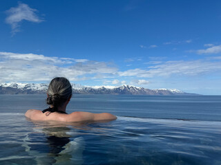 Plakat woman enjoying the view over the bay and the snow capped mountains in the distance while bathing in a geothermal hot pool