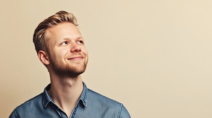 Obraz premium Smiling young Caucasian man looking upwards, wearing a denim shirt.