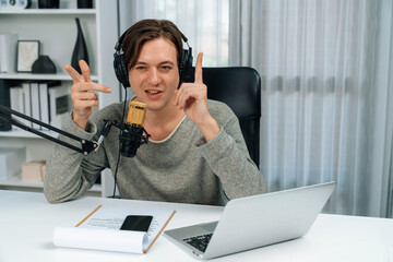 Host channel in smiling smart broadcaster recording, talking show with script and smartphone on desk on live social media, wearing headphones to record video streamer at modern home studio. Pecuniary.