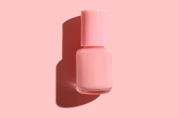 Pink glass container with nail polish on pink background.