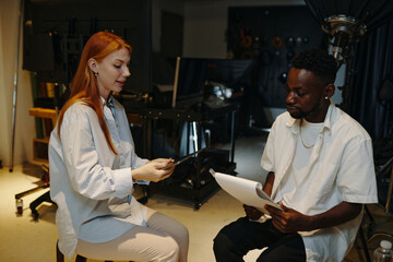 Professional woman and man analyzing documents and discussing project details in modern office setting. Diverse business setting with various office equipment present