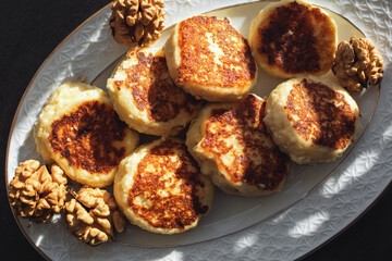 Vanilla nut cottage cheese pancakes ( syrniki or curd fritters) decorated with walnuts on white plate in sunny morning. High-protein breakfast ideas.