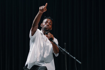 Performer passionately speaking on stage while pointing upwards, engaging the audience during...