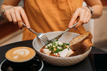 Woman eating tasty Shakshuka at cafe. Middle eastern traditional dish. Fried eggs with tomatoes and cup of coffee. Concept of easy breakfast. Food banner