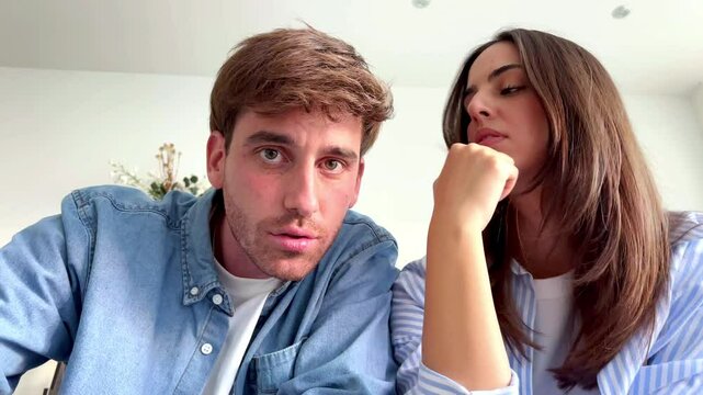 A young couple sits indoors on a comfortable sofa during their leisure time, appearing slightly frustrated and bored as they attempt to navigate an app and input a forgotten password