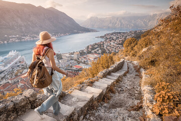 Female tourist descending ancient stone steps, savoring breathtaking view of Kotor bay at sunset in Montenegro