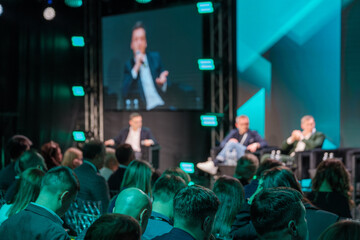 Vibrant business conference panel in progress with diverse audience listening attentively. Speakers on stage engage with participants, promoting collaboration and innovation in professional setting.
