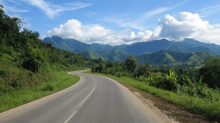 Naklejka premium Winding asphalt road meandering through vibrant green mountains under a bright blue sky dotted with fluffy clouds
