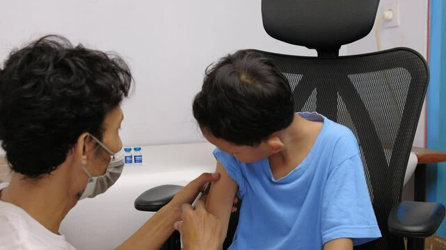 a male nurse injects a young boy with an immunization vaccine in a medical room
